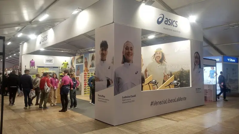 Stand ASICS con pannelli con foto di atleti e visitatori