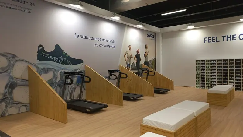 Area ASICS con scarpe esposte su gradini e tapis roulant