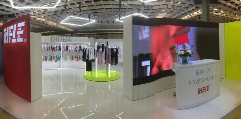 Stand bianco con schermo e abiti su piattaforma verde