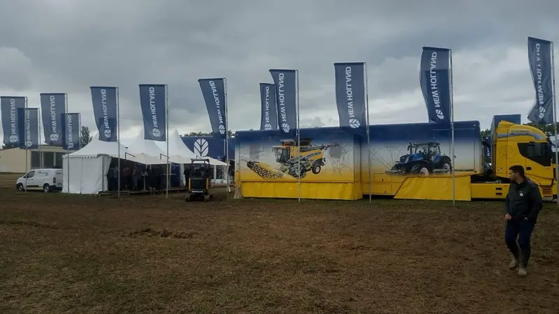 Area espositiva New Holland all'aperto con bandiere blu e camion