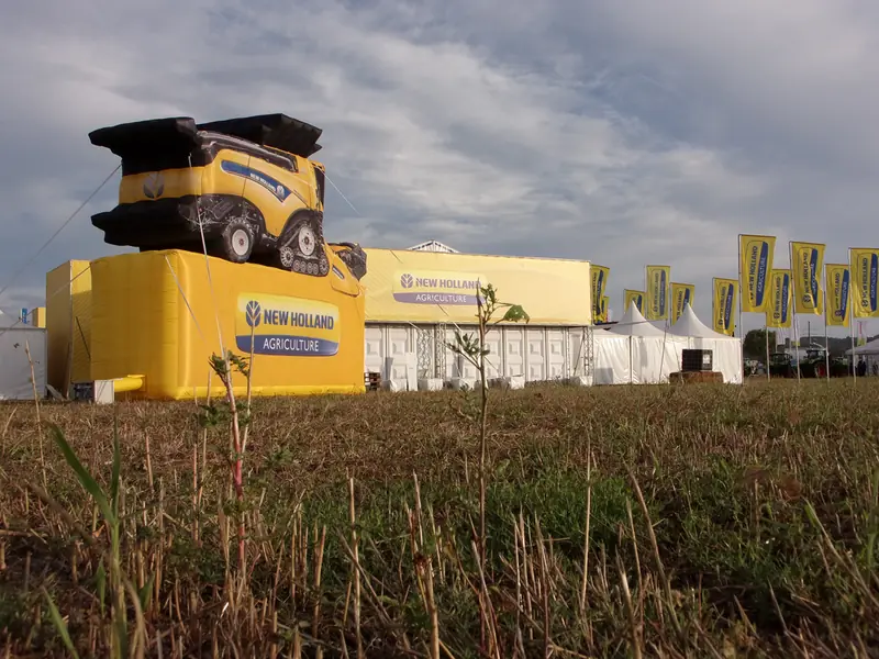 Struttura gialla New Holland con trattore sopra e campo in primo piano