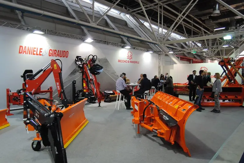 Stand con attrezzature arancioni, lame sgombraneve e persone