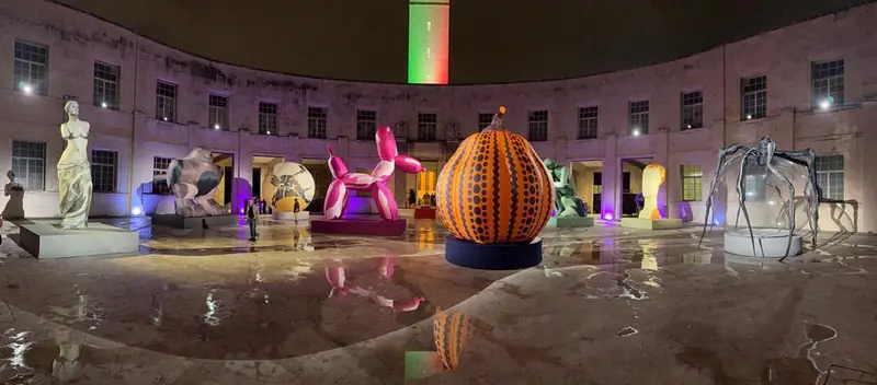 Allestimento serale in una piazza con sculture colorate illuminate, tra cui una grande zucca
