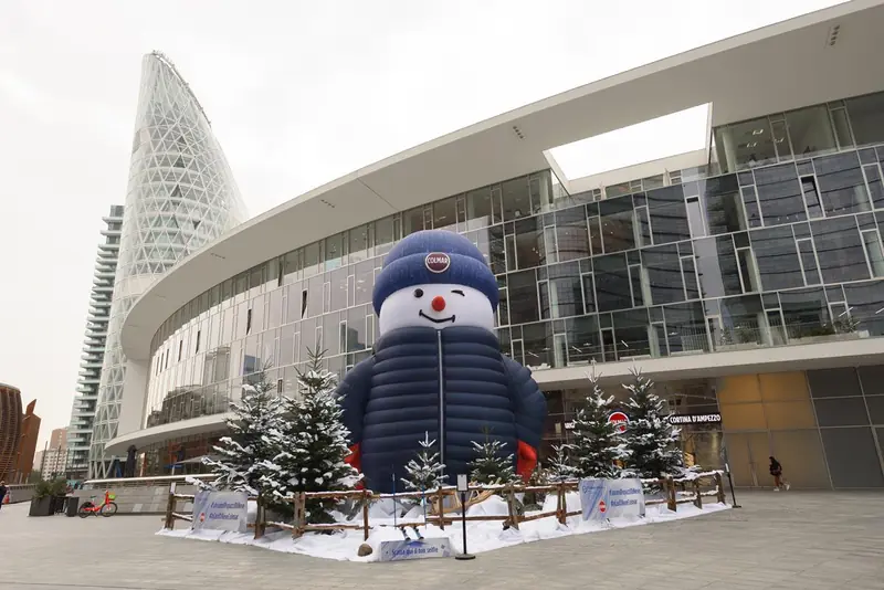 Pupazzo di neve gonfiabile gigante con piumino davanti a un edificio moderno