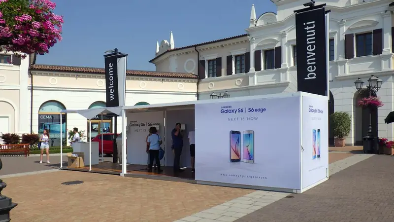 Stand bianco con grafiche per smartphone davanti a un edificio storico