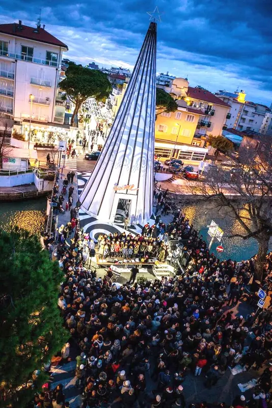 Folla davanti a un albero di Natale luminoso a forma di cono in una cittadina di mare