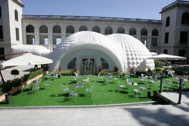 Struttura gonfiabile bianca a cupola con giardino e tavoli davanti a un palazzo storico