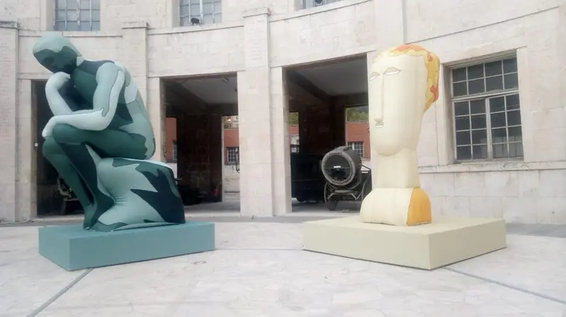 Sculture gonfiabili colorate davanti a un edificio: una figura seduta e una testa stilizzata