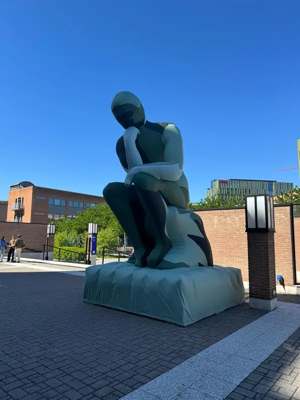 Scultura gonfiabile verde di una figura pensierosa in un cortile