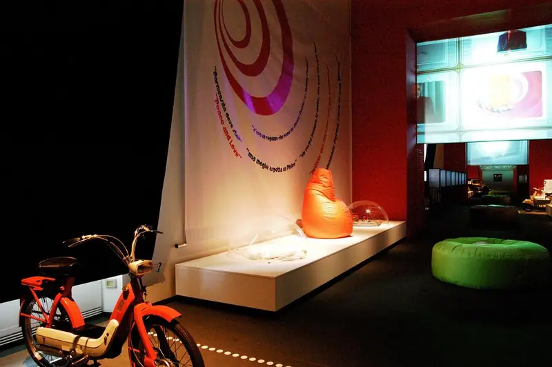 Allestimento con motorino rosso, puff arancione e pareti colorate