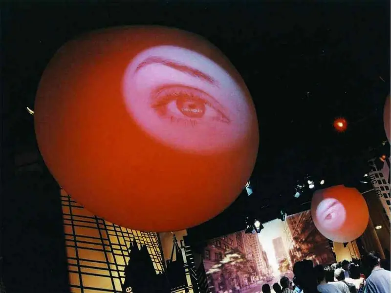 Sfera arancione con un occhio proiettato, sospesa in uno spazio espositivo