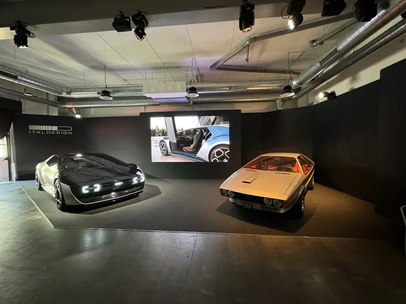 Sala espositiva scura con due auto d'epoca illuminate e schermo