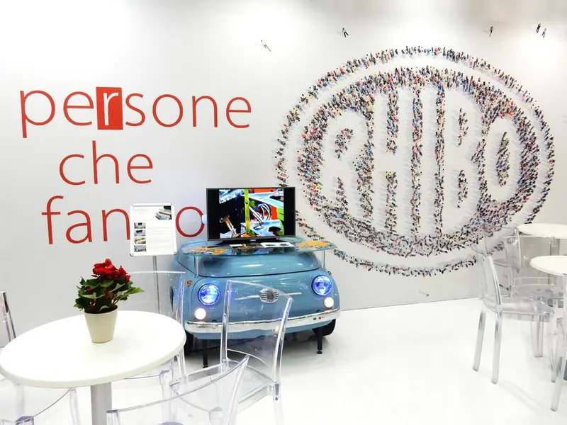 Stand bianco con parete grafica Rhibo e piccola auto azzurra