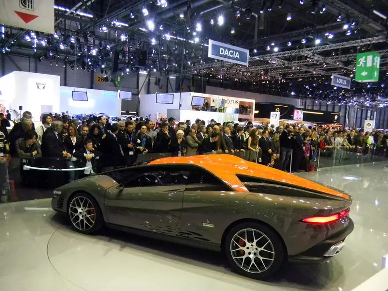 Auto sportiva arancione e grigia esposta davanti alla folla in un salone