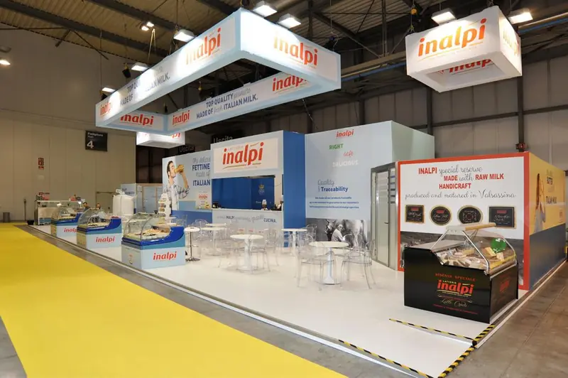 Stand Inalpi con insegne sospese e banco su pavimento giallo
