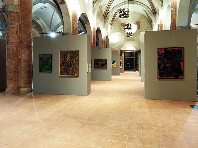 Mostra d'arte in una chiesa con volte in mattoni e dipinti su pareti grigie
