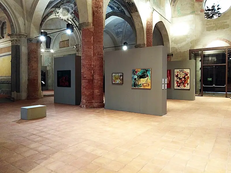 Mostra di dipinti in una chiesa con pannelli espositivi grigi, vista alternativa