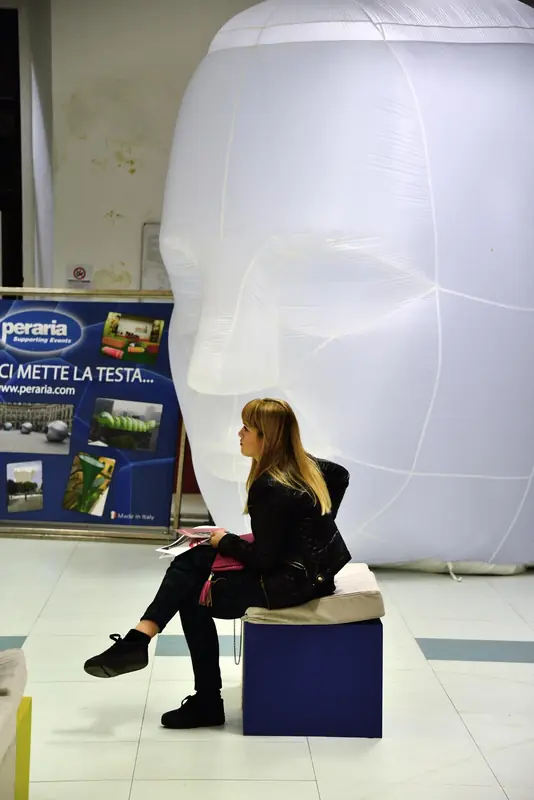 Testa gonfiabile bianca con una persona seduta su un cubo in un'area fieristica