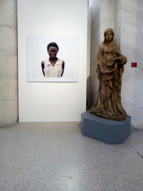 Ritratto fotografico accanto a una statua lignea in una sala bianca
