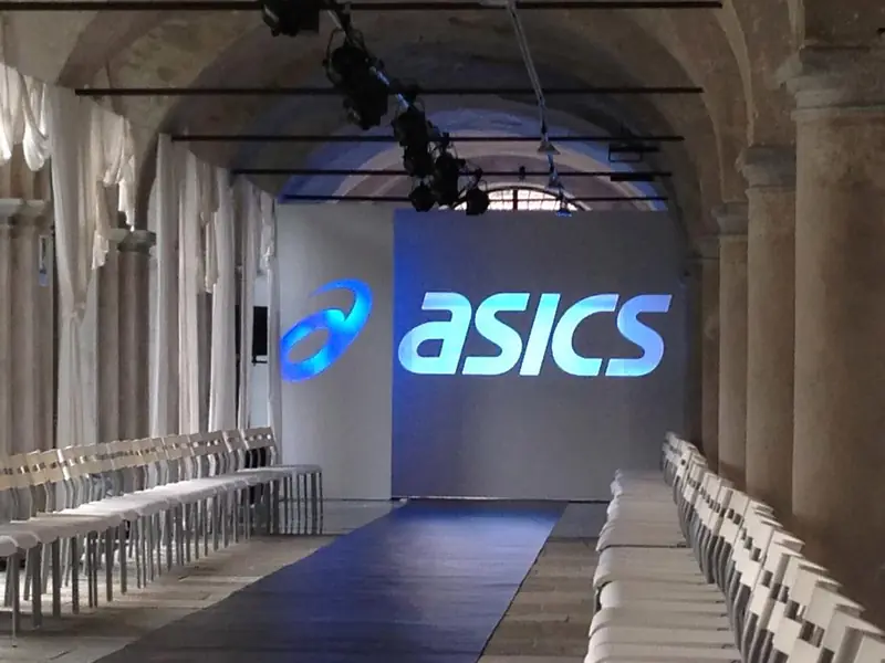 Passerella con sedie e logo ASICS in uno spazio storico con volte