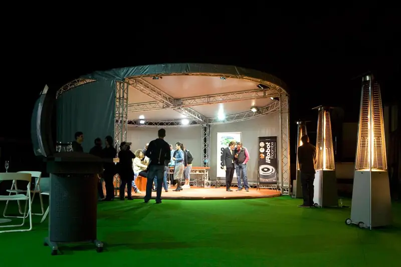 Palco circolare illuminato di notte su prato sintetico con stufe a fungo
