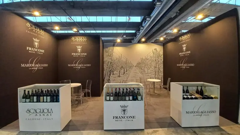 Stand scuro con bottiglie esposte su banchi bianchi di Scagliola, Francone e Marco Calcagno